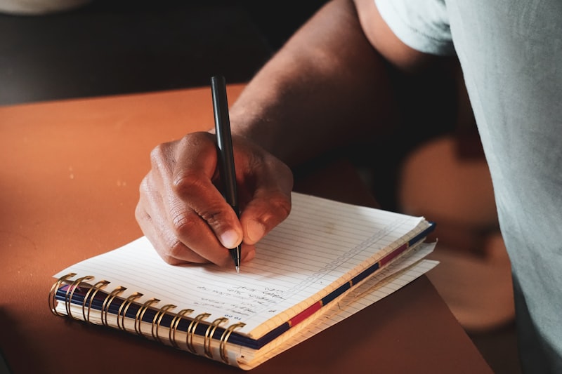 Person writing out assignment requirements in a notebook with a pen